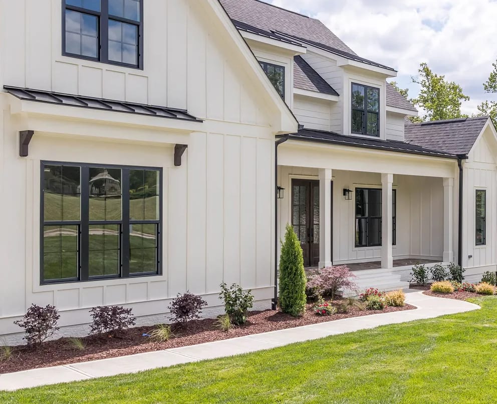 Front of a white board-and-batten home with black-framed windows and a covered porch